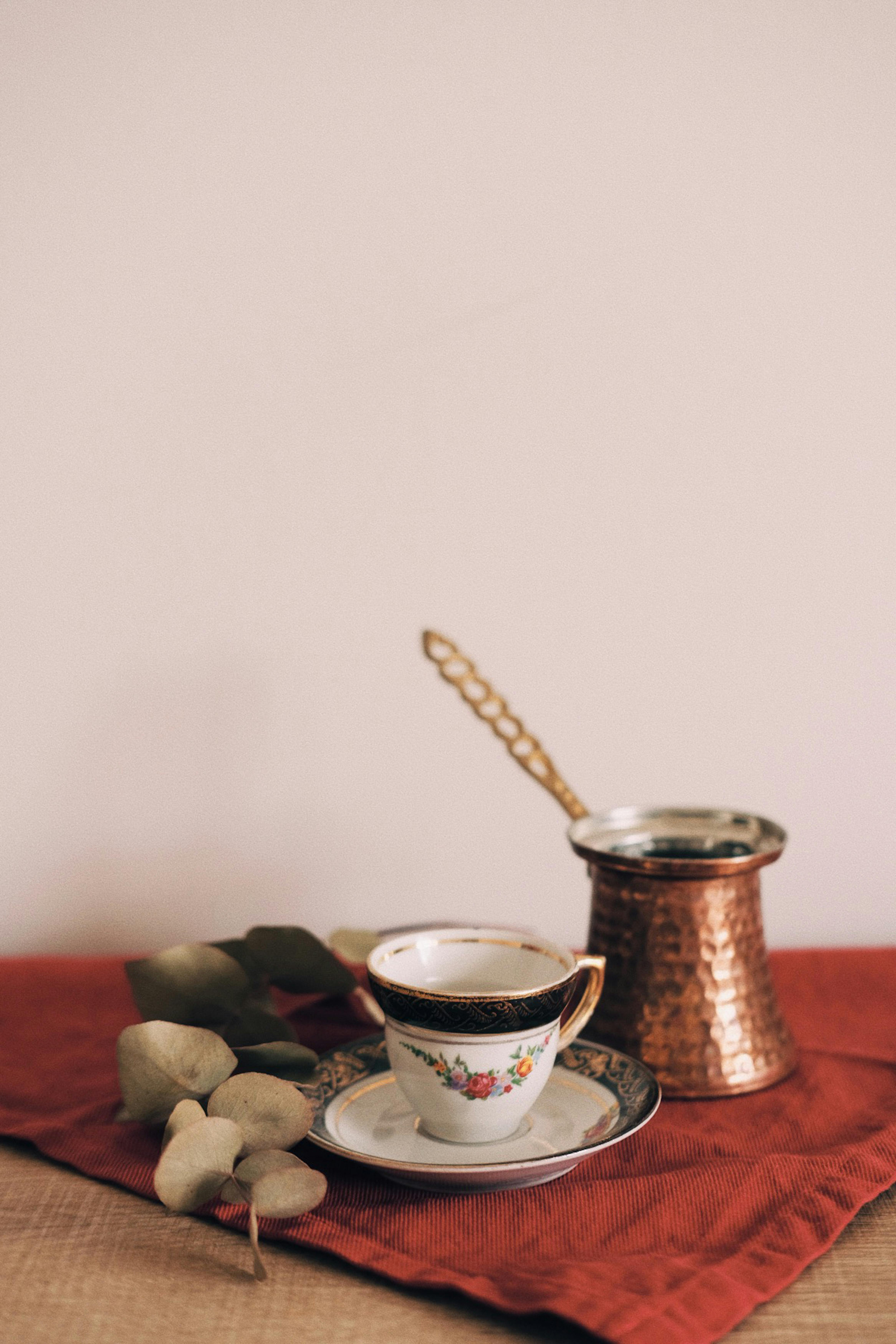 Elegant coffee scene with floral cup, red cloth, and copper pot for a warm atmosphere.