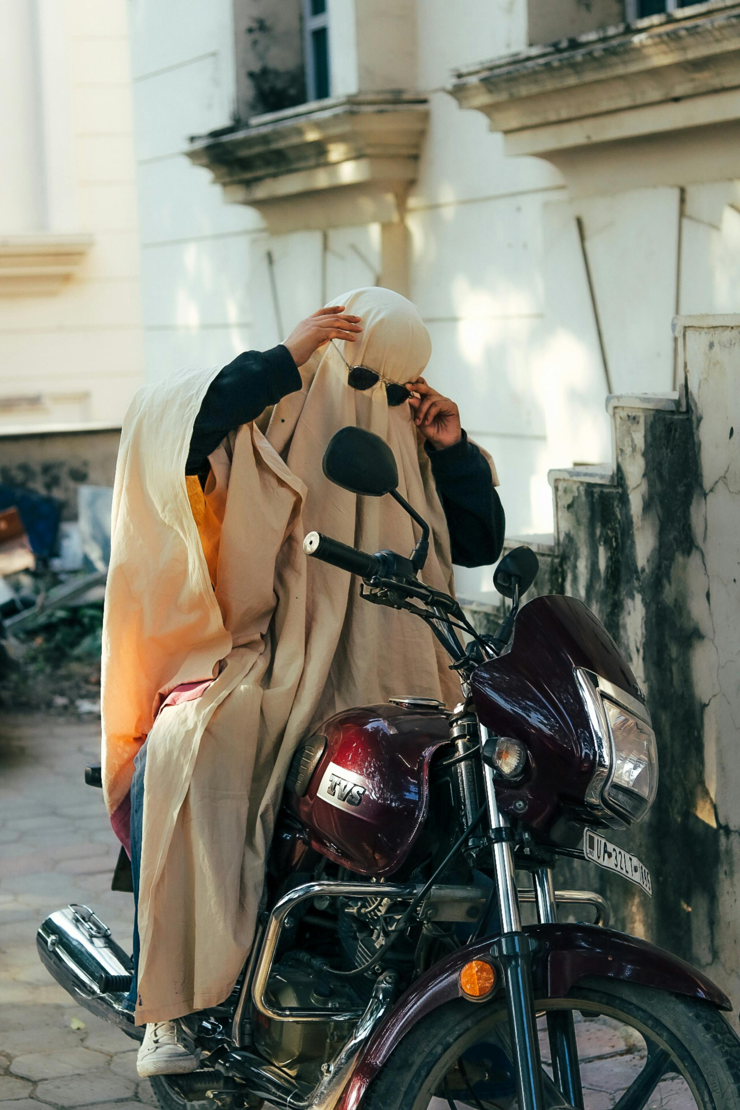 A mysterious ghostly figure covers itself while sitting on a motorcycle, adding an eerie touch to the urban street scene in Lucknow.