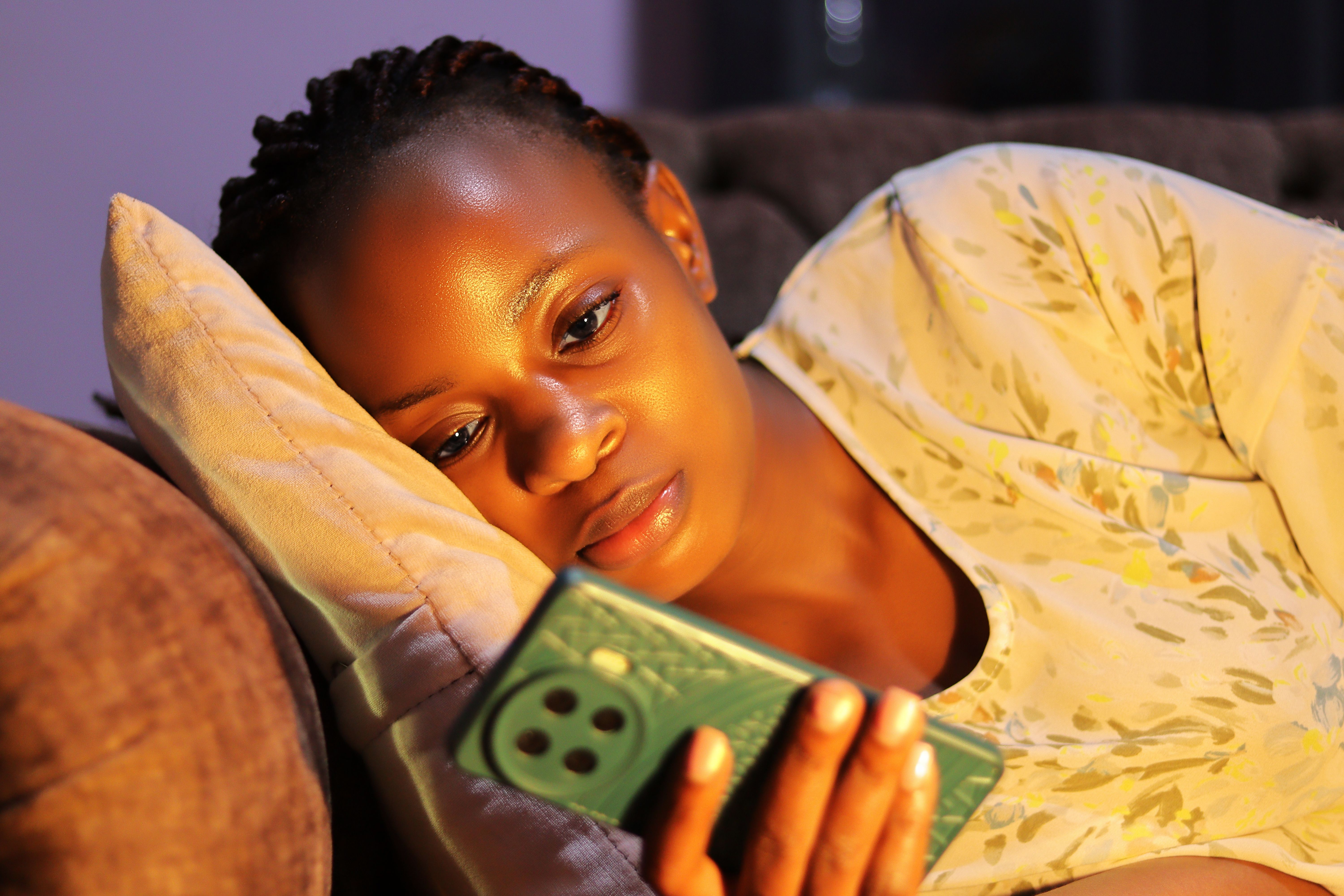 A young woman lying on a couch, engrossed in her smartphone at night.