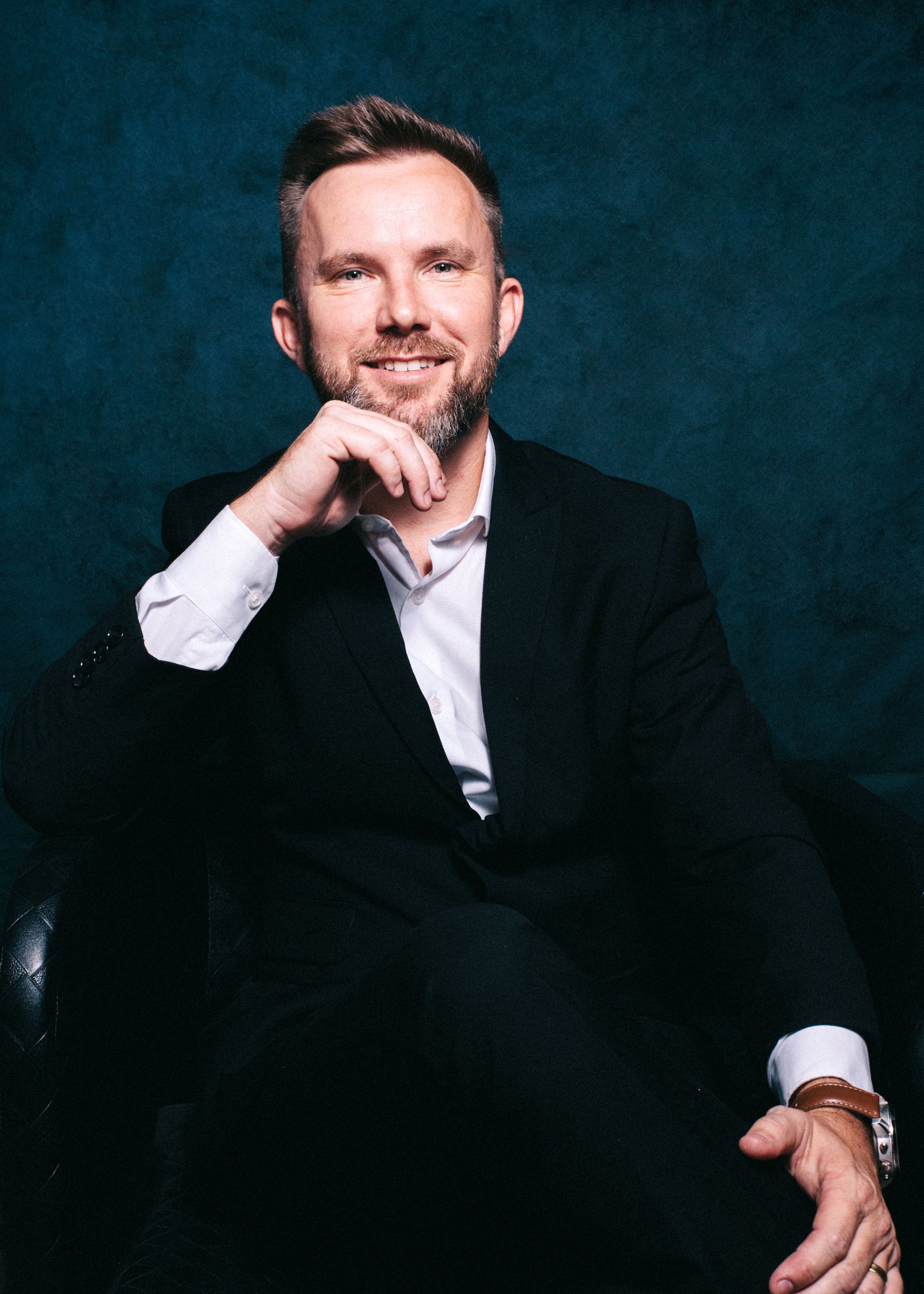 Portrait of a confident man in a dark suit with a thoughtful expression, indoors.