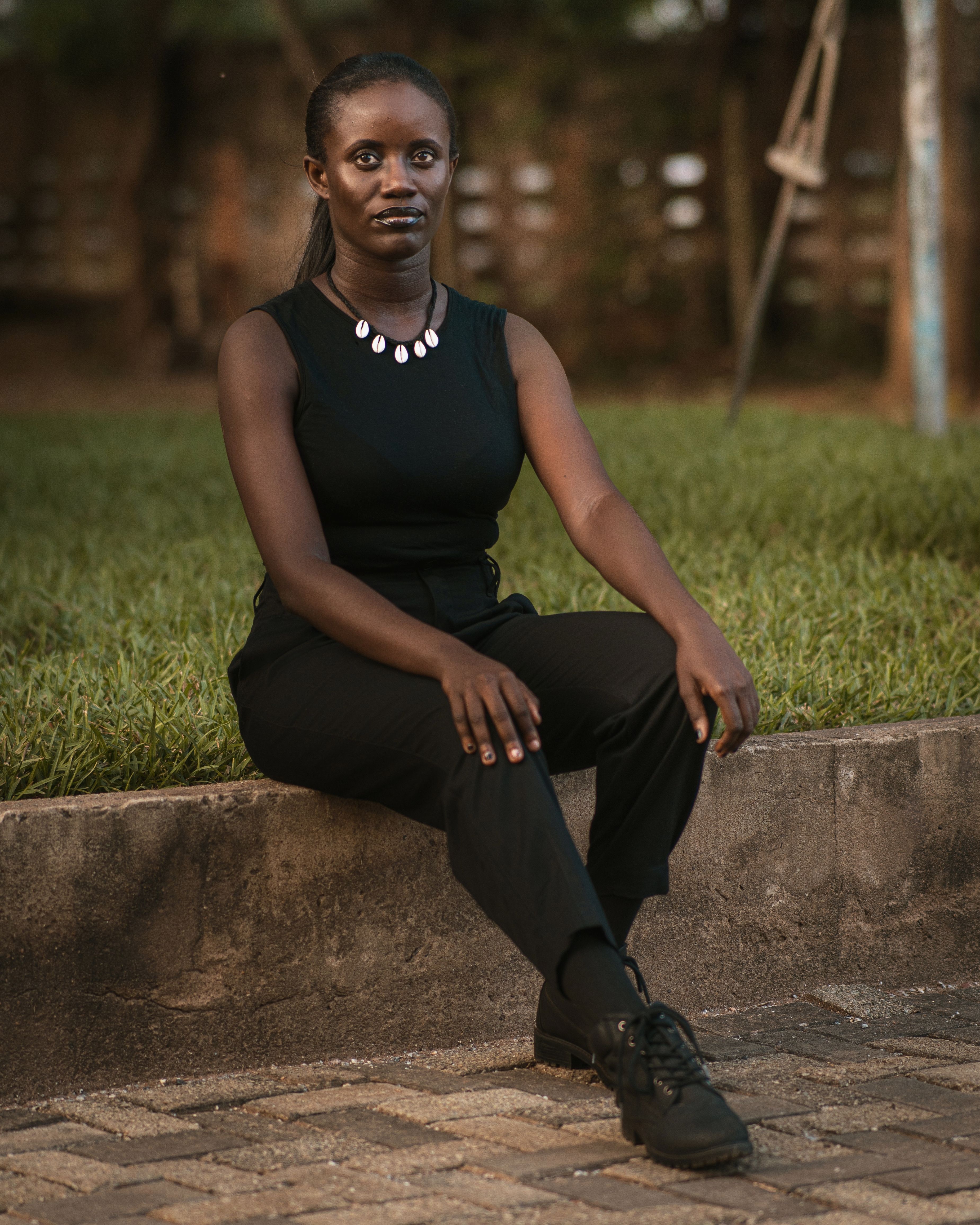 Elegant woman in all-black outfit sitting on a stone wall outdoors, exuding confidence and style.