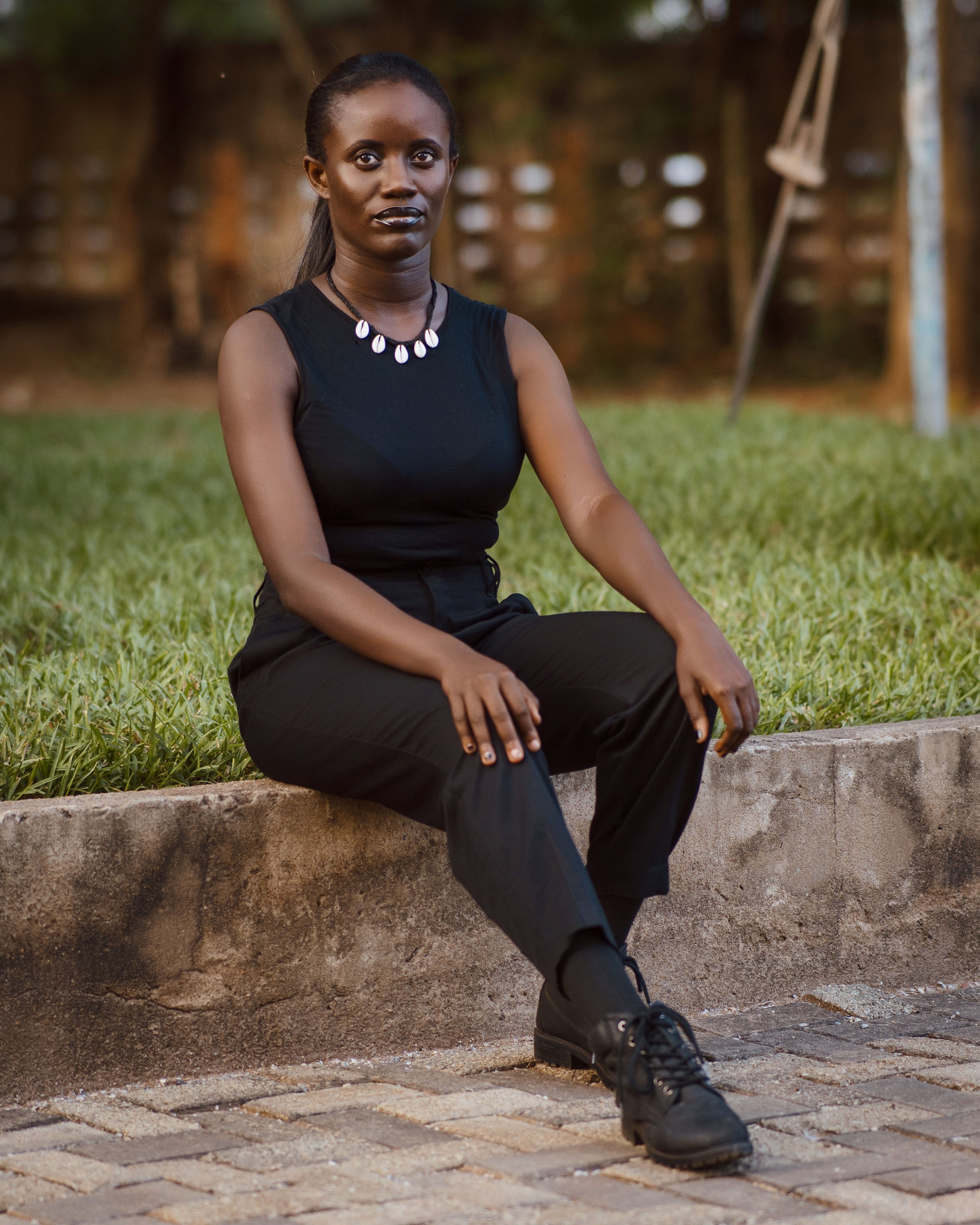 A confident woman in black attire sitting outdoors on a stone ledge during the day.