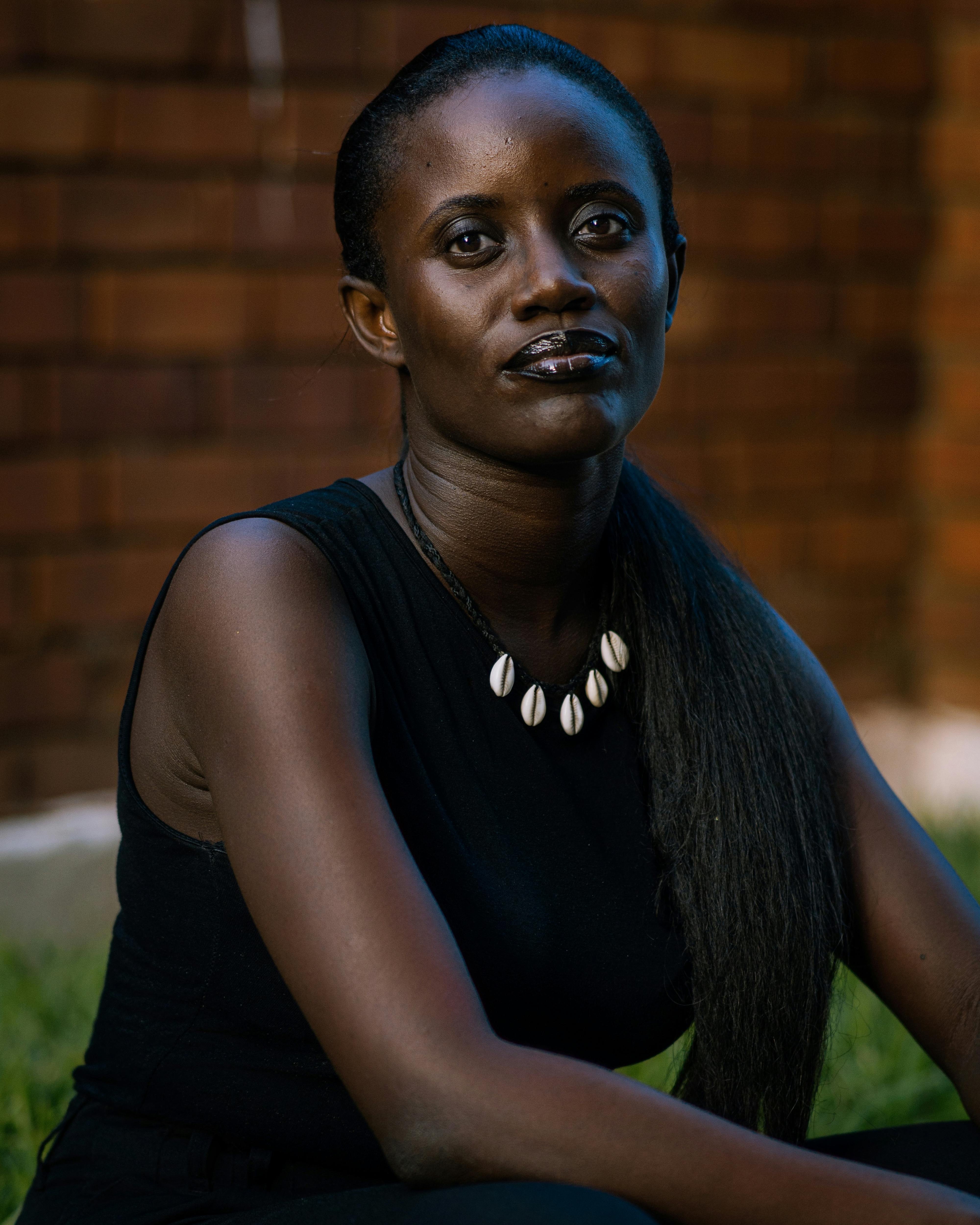 A thoughtful woman in a black dress sitting outdoors by a brick wall.