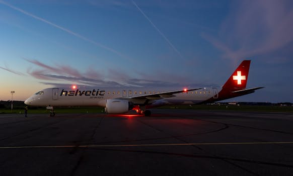 Helvetic Airways Embraer jet parked on airport tarmac during twilight, sky with soft hues.
