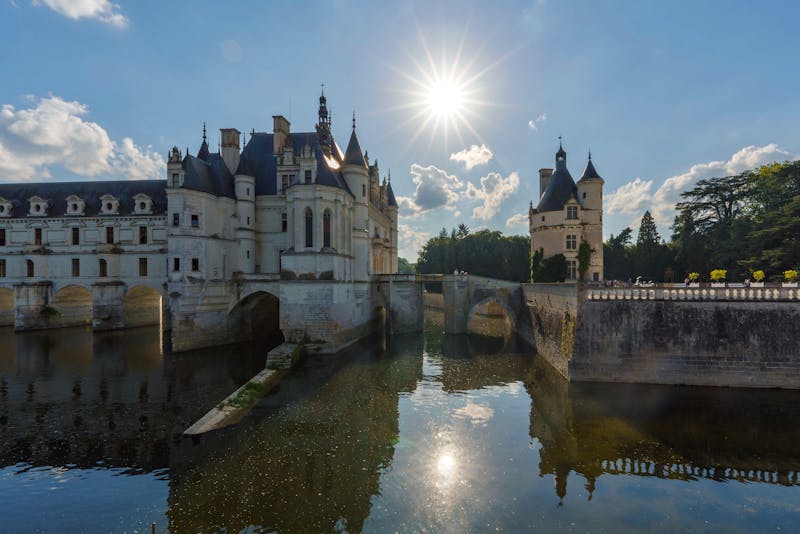 Stunning view of Château de Chenonceau with sunburst and reflections on the river Cher.