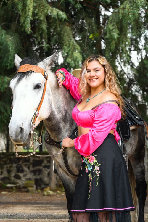 Free Young woman in vibrant dress posing happily with a horse in a natural setting. Stock Photo