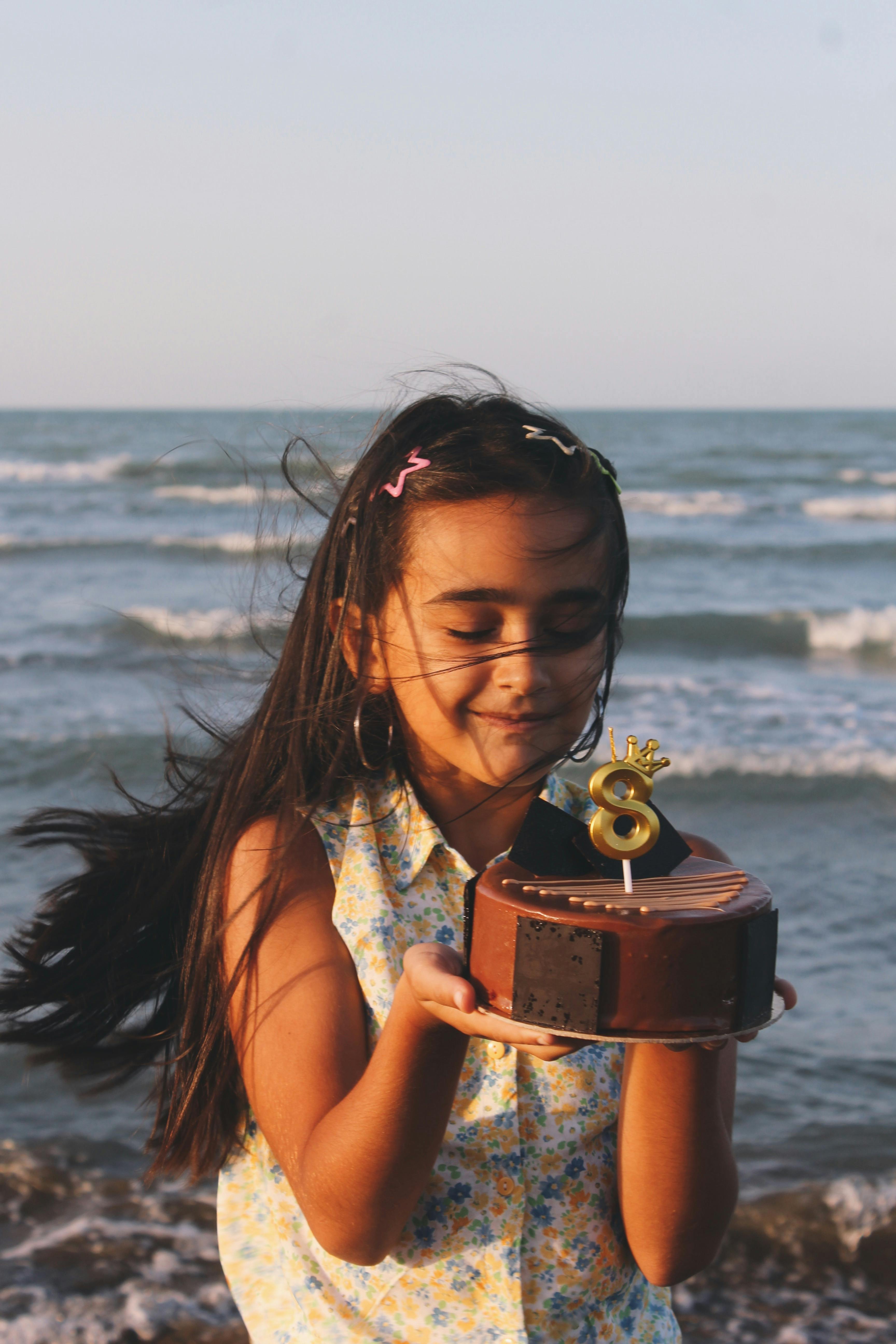 Girl holding a birthday cake with a number six candle on a beach.