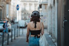 Back view of a young woman with headphones walking in an urban street, enjoying music.