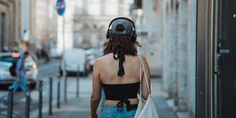 Back view of a young woman with headphones walking in an urban street, enjoying music.