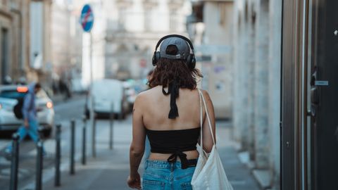 Back view of a young woman with headphones walking in an urban street, enjoying music.