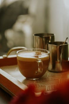 Close-up of a latte with milk frother on a wooden tray, warm ambiance.