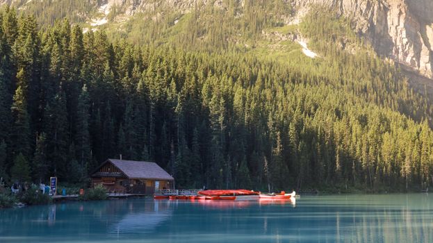 A tranquil lake in Calgary with vibrant red canoes and a rustic dock, surrounded by lush forest.