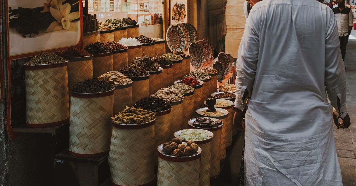 Vendors serve customers from colorful, brightly lit wooden food stalls at a crowded outdoor night market in Dubai.