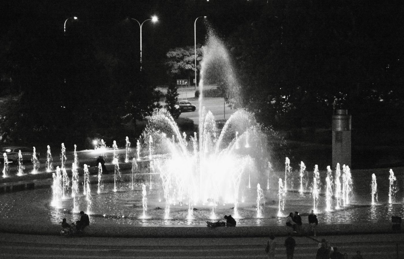 Black and white image of a lit fountain in Warsaw, Poland, during night time.