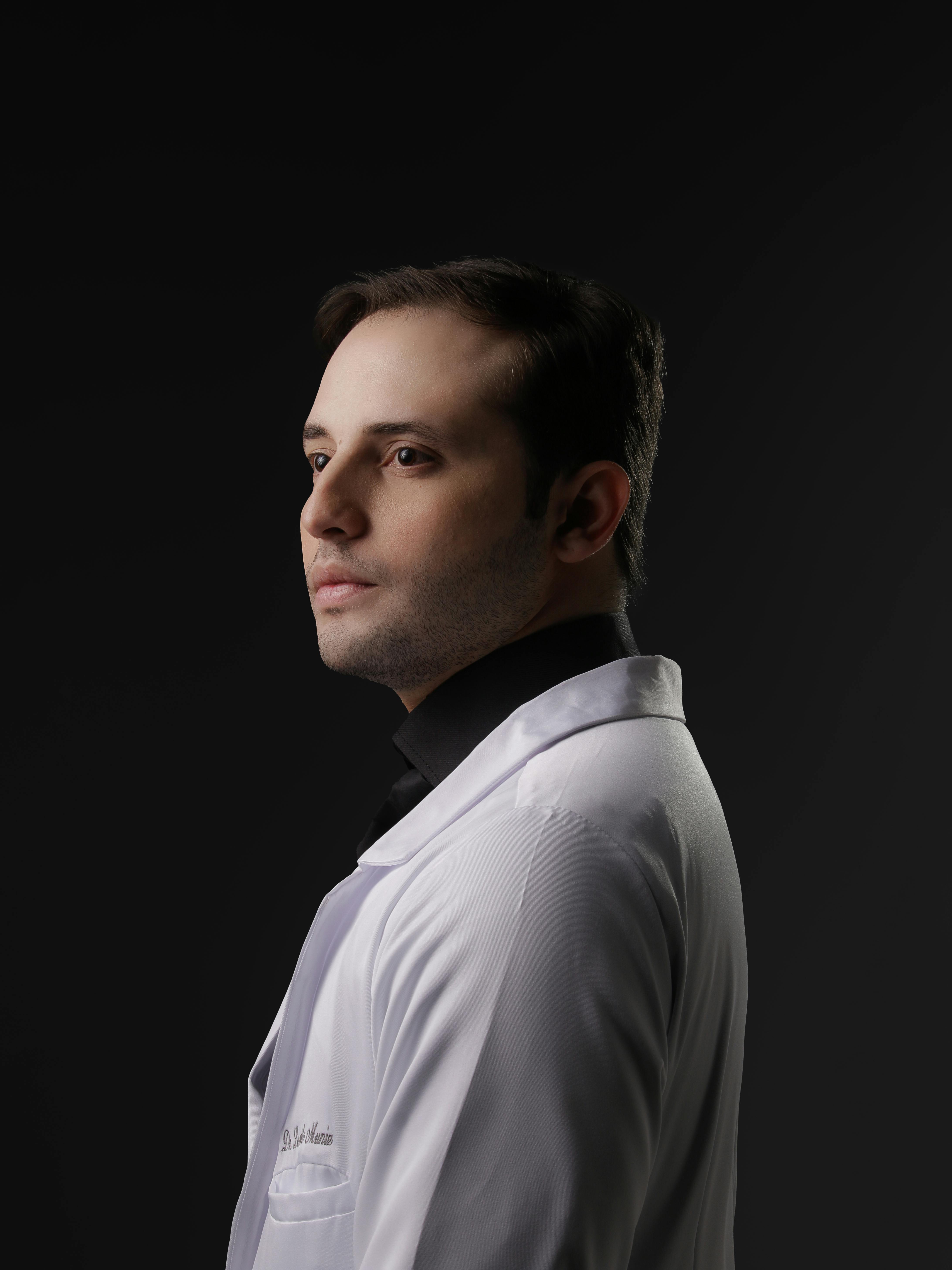 Side profile of a male doctor in a white coat against dark backdrop.