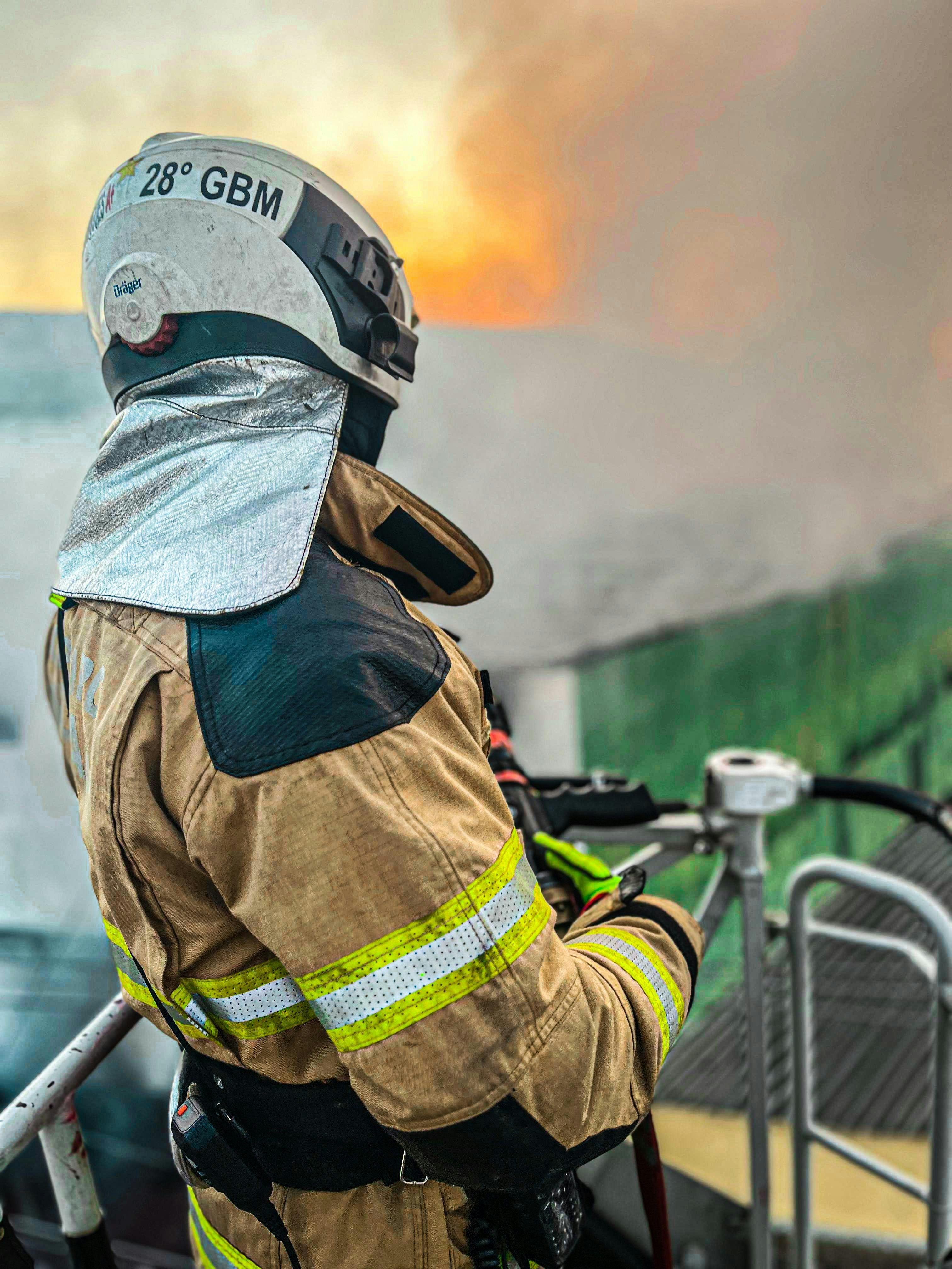 Firefighter in protective gear fighting a building fire with a hose.