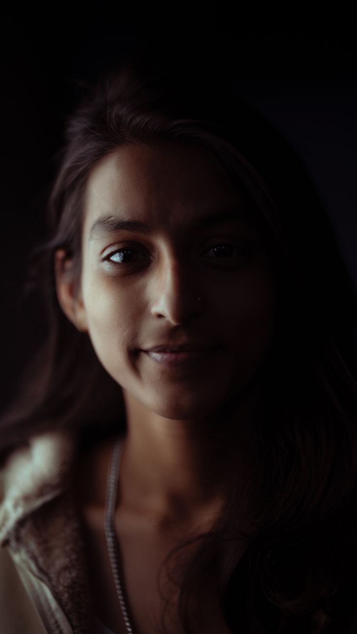Intimate close-up portrait of a young woman in soft lighting, featuring a serene expression.