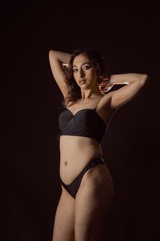 A stylish portrait of a woman posing confidently in a dark studio setting, showcasing elegance.