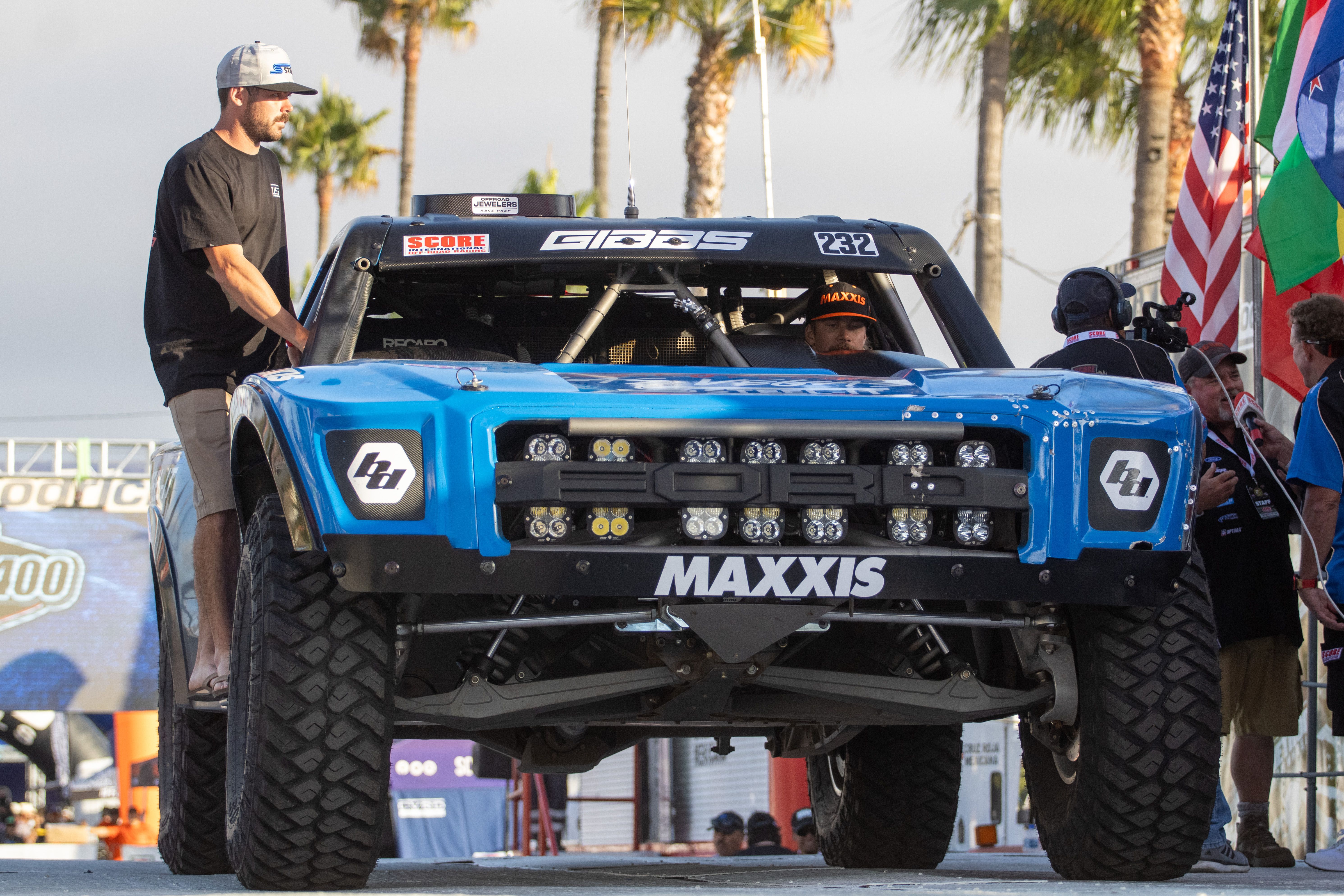 Dynamic image of a racing truck at an off-road competition with spectators and flags.