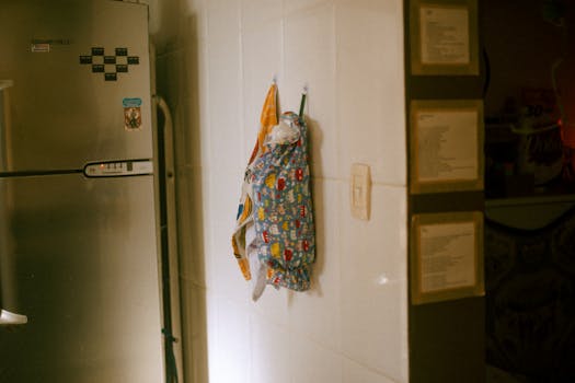 A domestic kitchen scene showing a decorated apron hanging beside a stainless steel fridge.