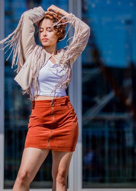 A stylish woman poses confidently outdoors wearing fringe jacket and skirt.