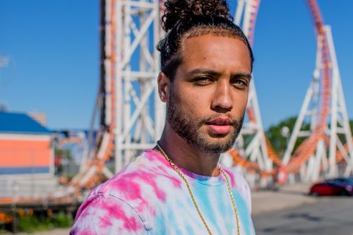 Free A young man with casual style poses in front of an amusement park ride on a sunny day. Stock Photo