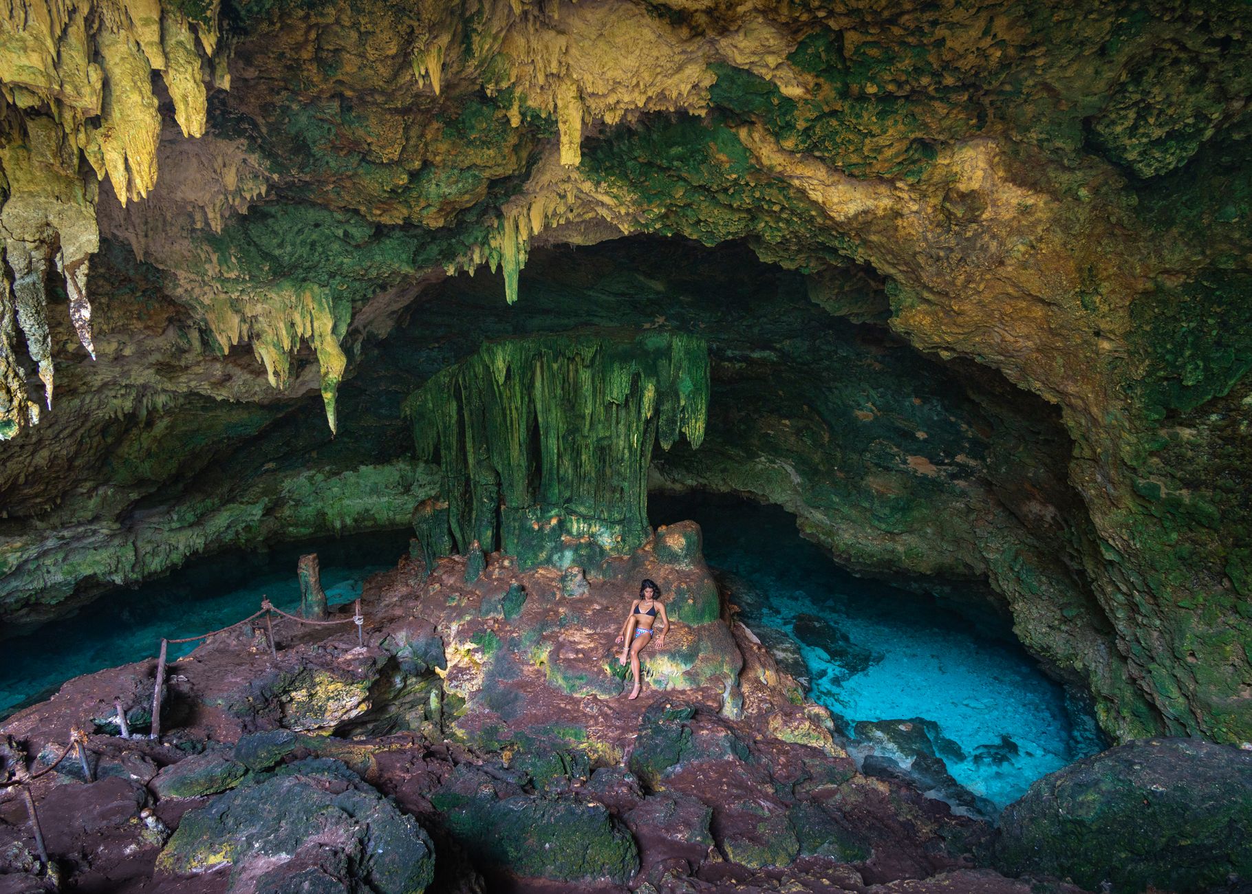 A person exploring a colorful cave with vibrant stalactites and a serene pool.