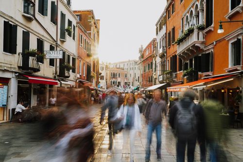 Free Blurred motion captures the energy of people walking through a vibrant Venetian street at sunset. Stock Photo
