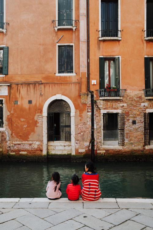 Free Family sitting by a scenic canal in Venice, Italy, enjoying a peaceful autumn day. Stock Photo