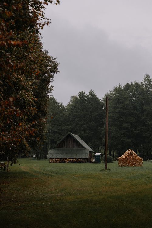 Free A peaceful rural landscape featuring a wooden barn and stacked firewood under overcast skies. Stock Photo