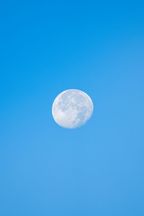 Free A bright moon visible against a clear blue sky during the day. Stock Photo