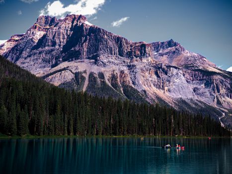 A breathtaking view of a serene lake surrounded by majestic Rocky Mountains and forest.