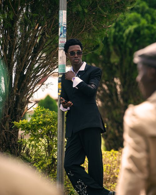 Free Fashionable man in sunglasses and suit leaning against a street post, exuding confidence in a city environment. Stock Photo