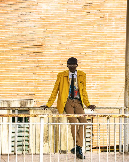 Free Fashionable man leaning on railing against urban backdrop in bold yellow jacket. Stock Photo