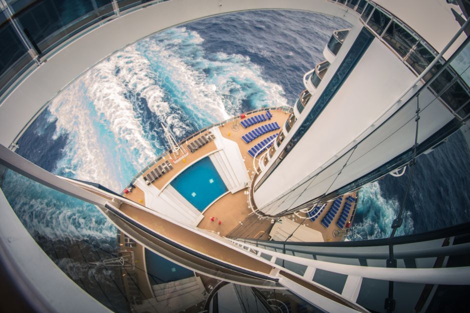 Bovenaanzicht van het zwembaddek van een cruiseschip met ligstoelen en zog in zee