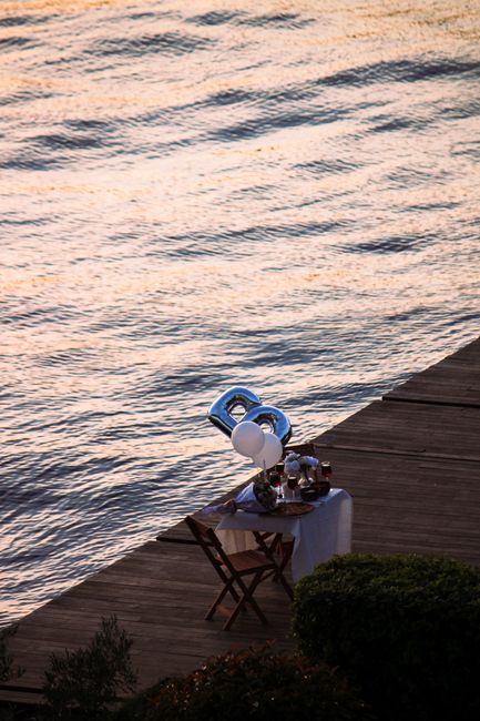 Fotomural Encantadora configuración de cena romántica junto al agua con globos y vajilla al atardecer.