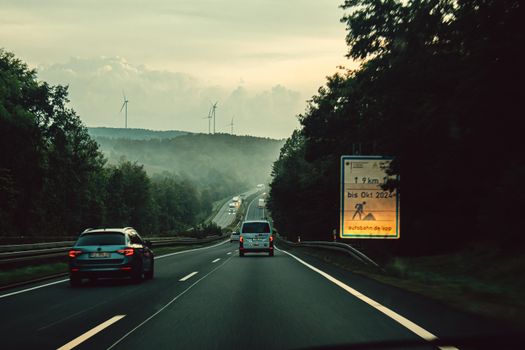 A calm drive along a misty highway with visible wind turbines and forest surroundings.