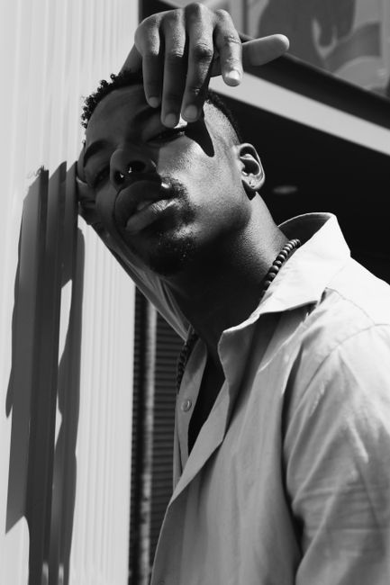 Black and white portrait of a man posing with a nose ring and relaxed expression.