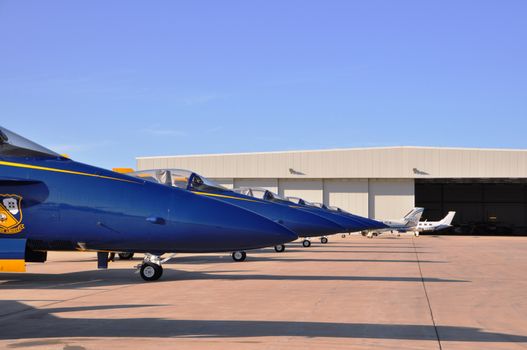 Blue fighter jets aligned on the tarmac in front of an aircraft hangar on a clear day., free online jigsaw puzzle on JigsawPuzzlesFreeOnline.org