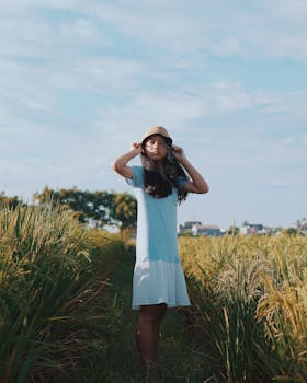 晴朗的天空下，一名身穿蓝色连衣裙的年轻女子站在稻田里