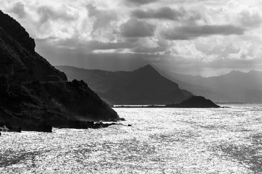 Stunning black and white photo of a rocky coastline under dramatic clouds.