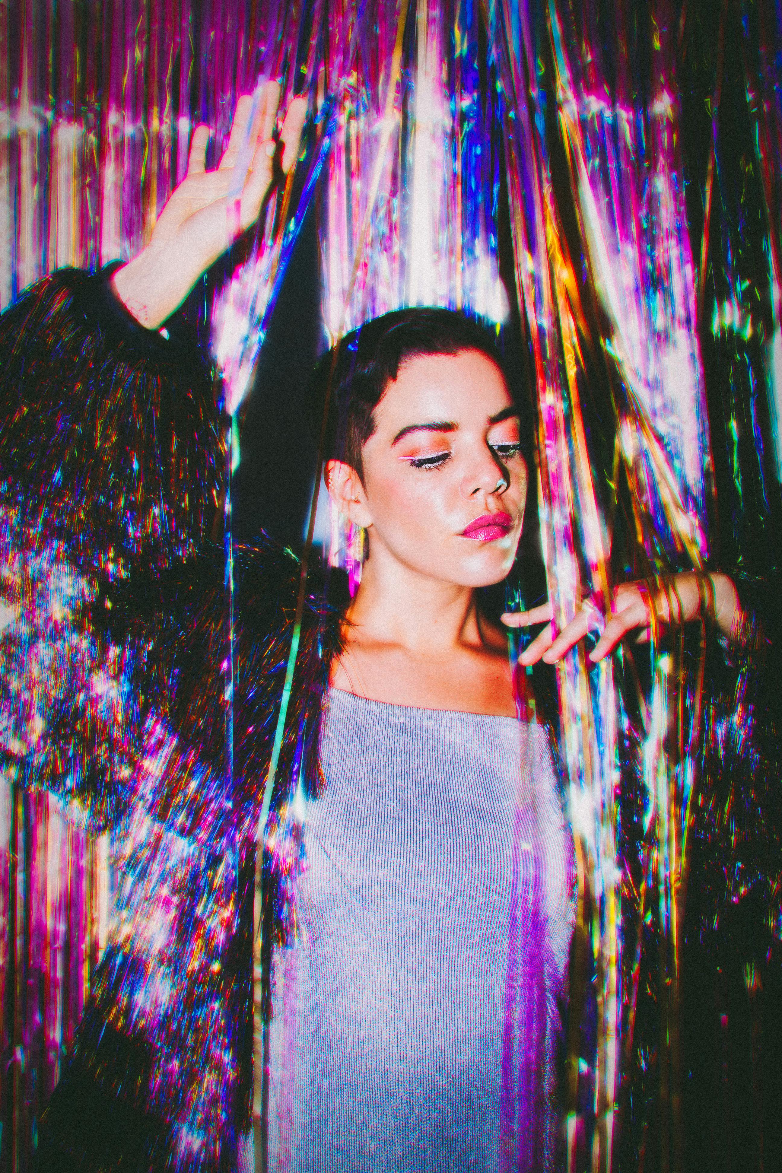 A woman poses with a shimmering, iridescent backdrop creating a vivid, artistic scene.