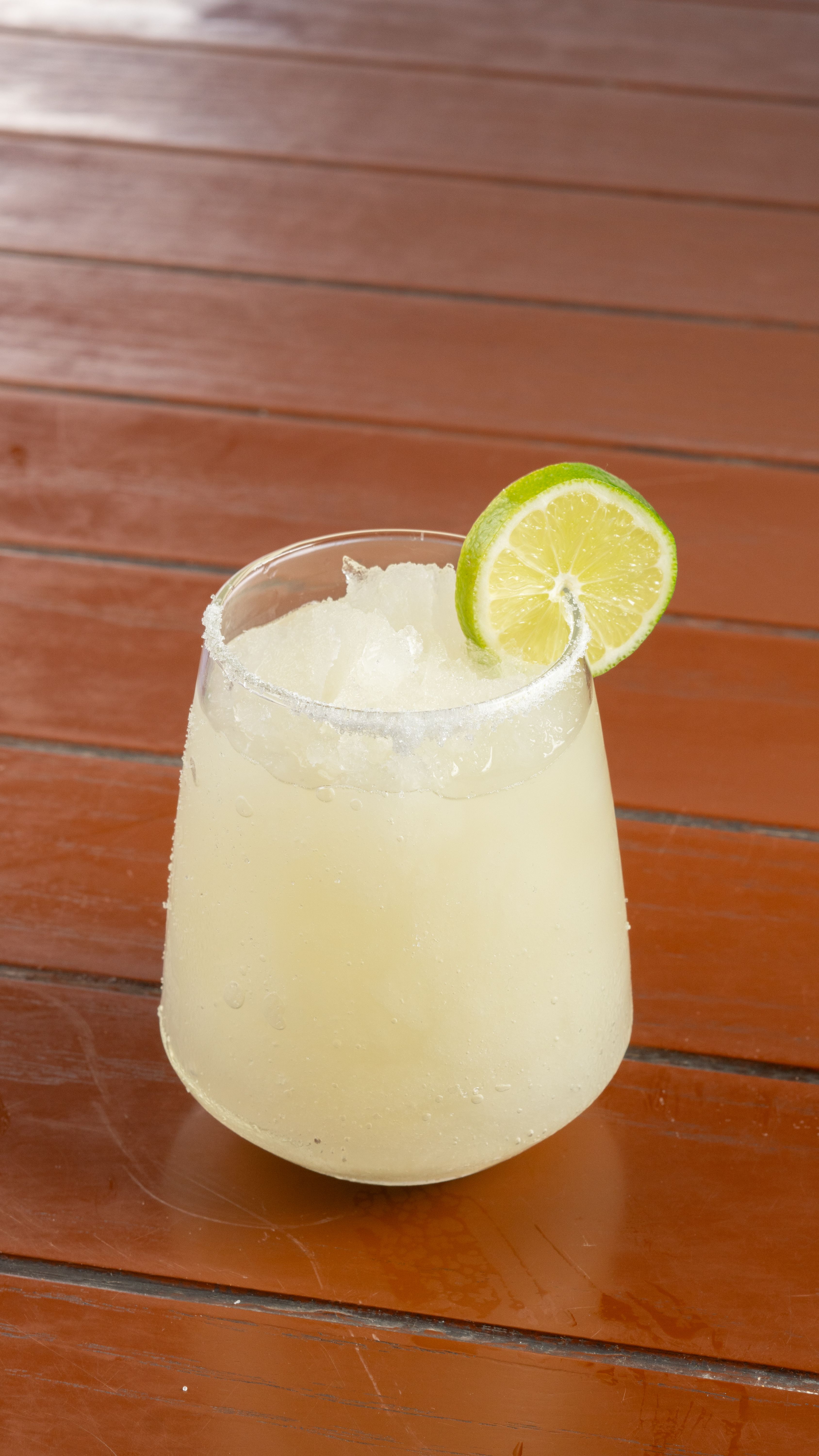 A chilled margarita topped with lime on a wooden table, perfect for summer vibes.