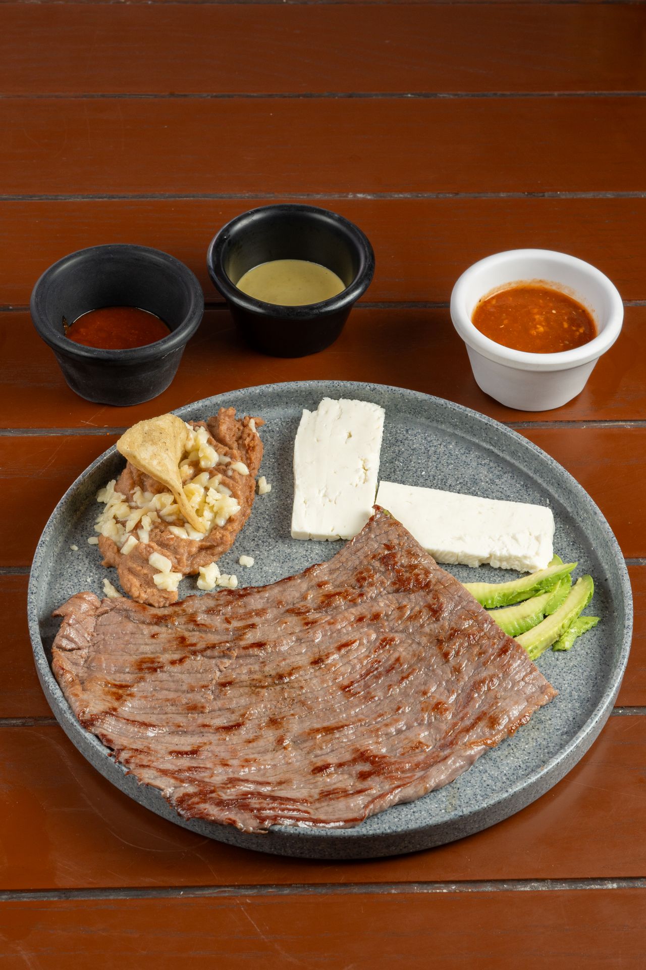 Grilled Mexican carne asada beef with avocado, cheese and sauces on a rustic table
