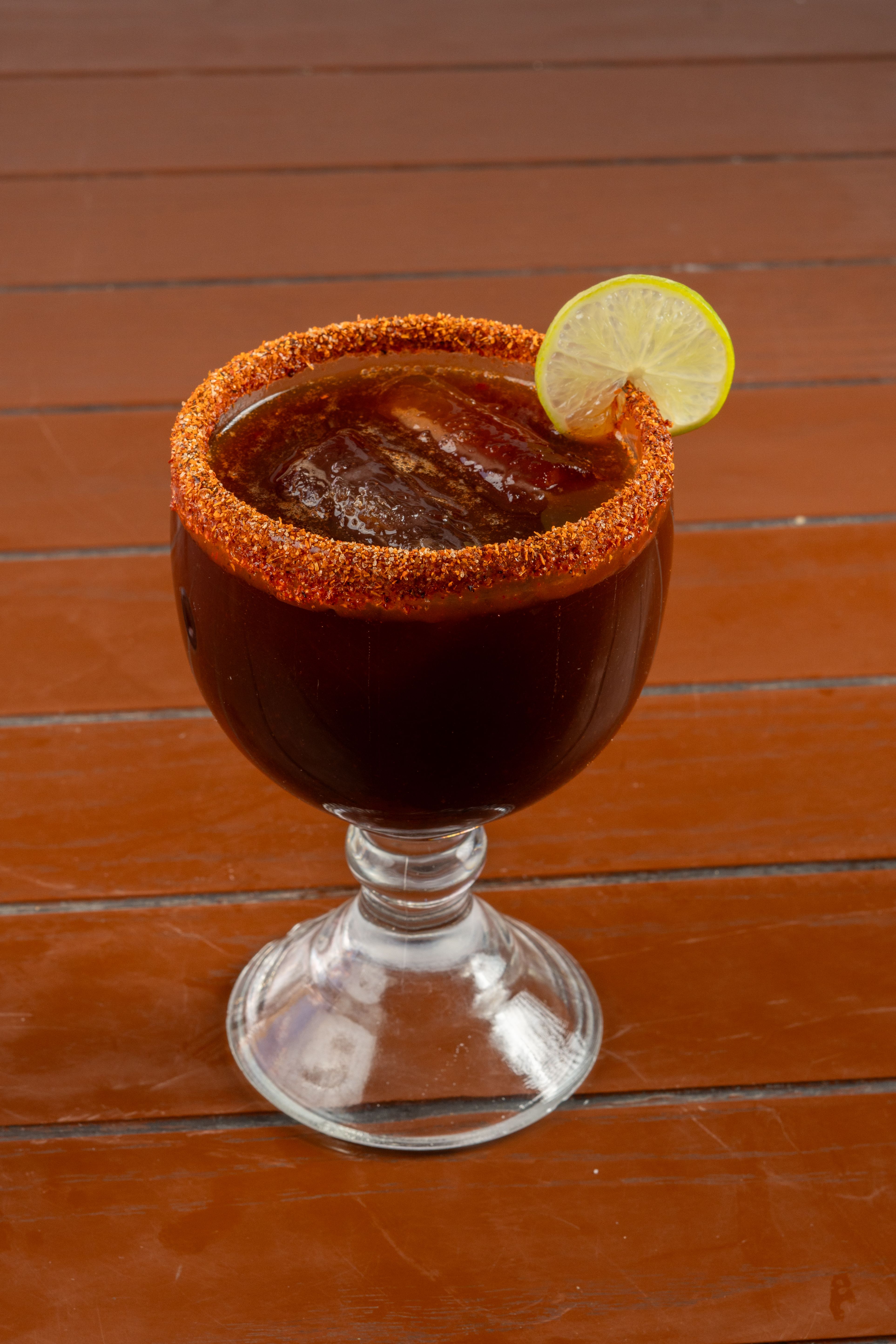 Chili-rimmed michelada with lime garnish on a wooden table in Puerto Escondido