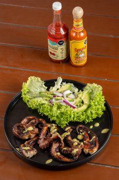 Delicious grilled octopus salad with lettuce and hot sauces on a wooden table, ready to serve.