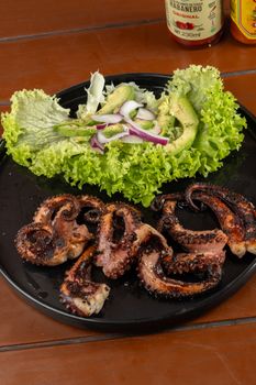 Delicious grilled octopus served with leafy greens, avocado, and onions.