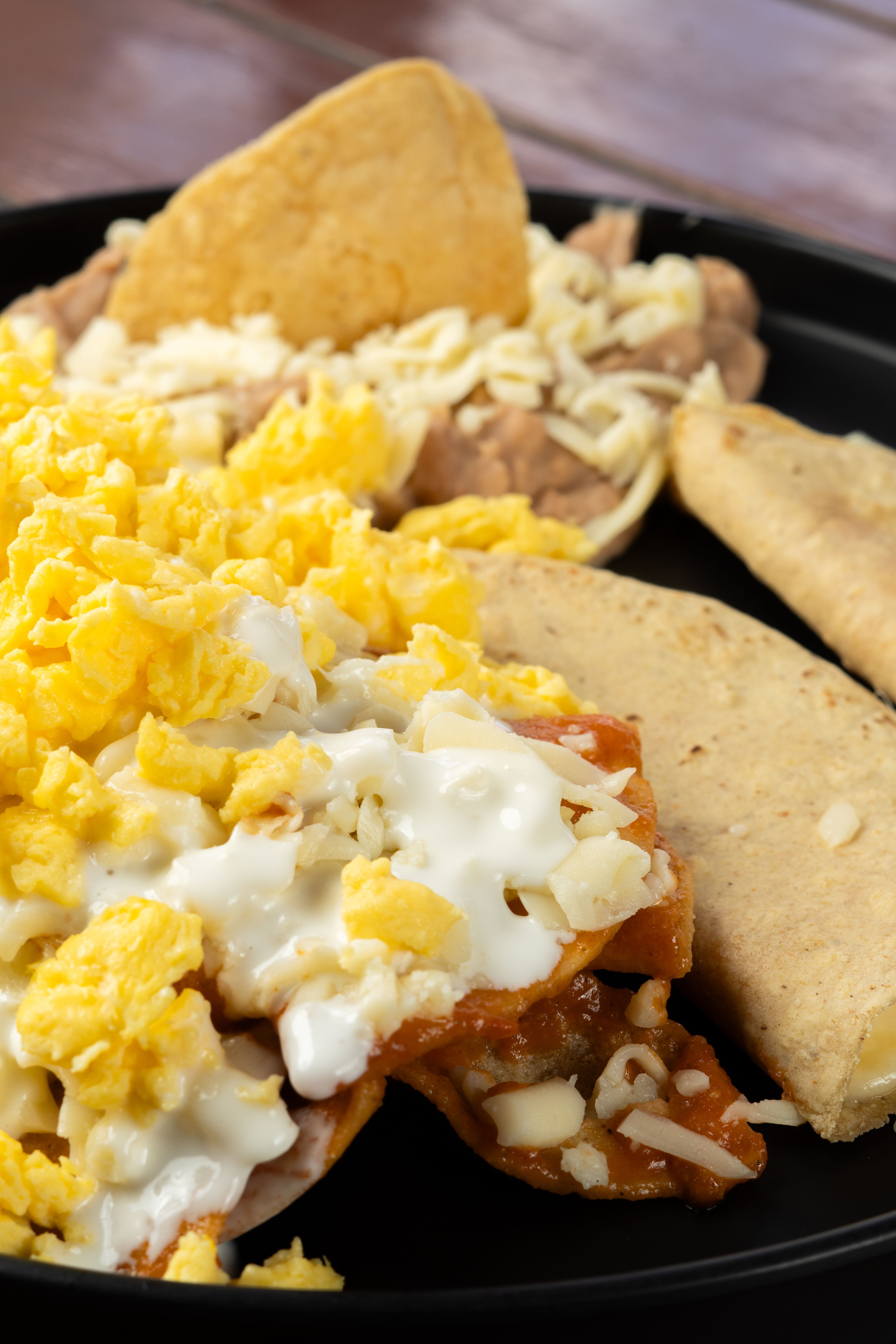 Appetizing meal featuring scrambled eggs, tacos, and cheese on a black plate.