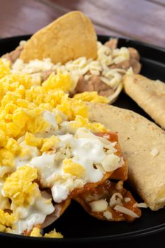 Appetizing meal featuring scrambled eggs, tacos, and cheese on a black plate.