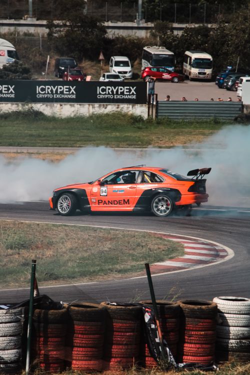 Free Dynamic shot of an orange race car drifting on a track. Smoke adds a thrilling effect. Stock Photo